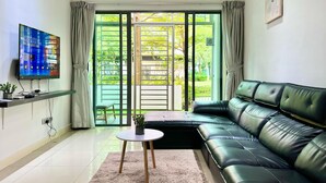 Un salon avec un canapé en cuir noir, un téléviseur à écran plat posé sur un meuble, une petite table ronde et une porte-fenêtre coulissante donnant sur un balcon.
