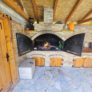 Un camino in pietra con un fuoco acceso, panche in legno e una porta di legno con maniglia.
