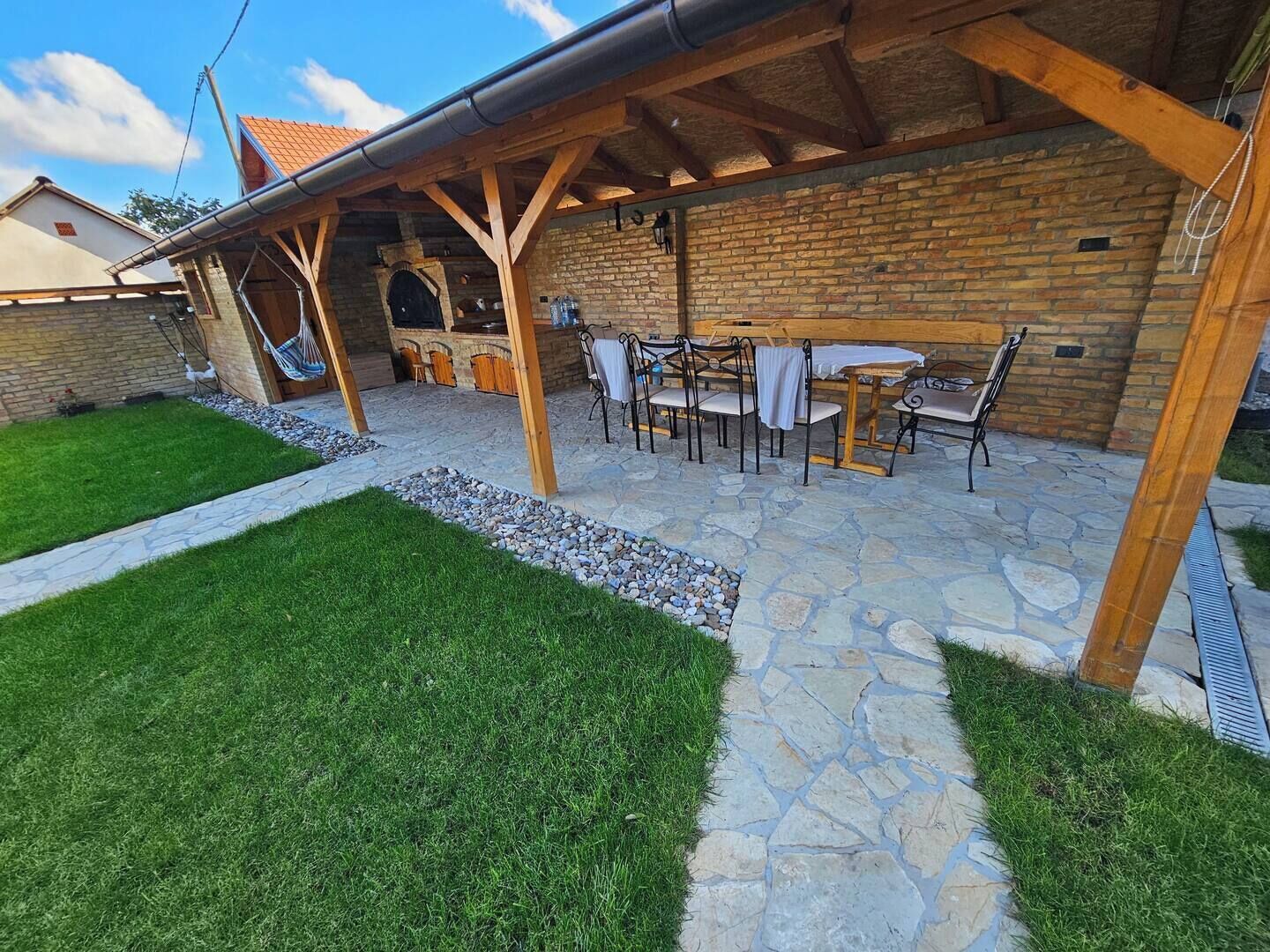 Eine überdachte Terrasse im Freien mit Steinböden, einer Ziegelwand und einer Holz-Pergola.