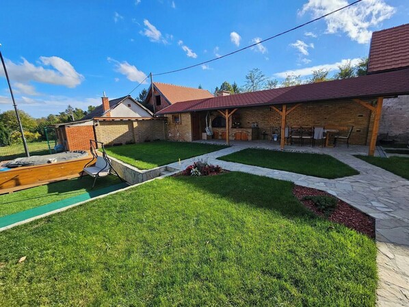A backyard with a wooden deck, a trampoline, and a brick patio area.