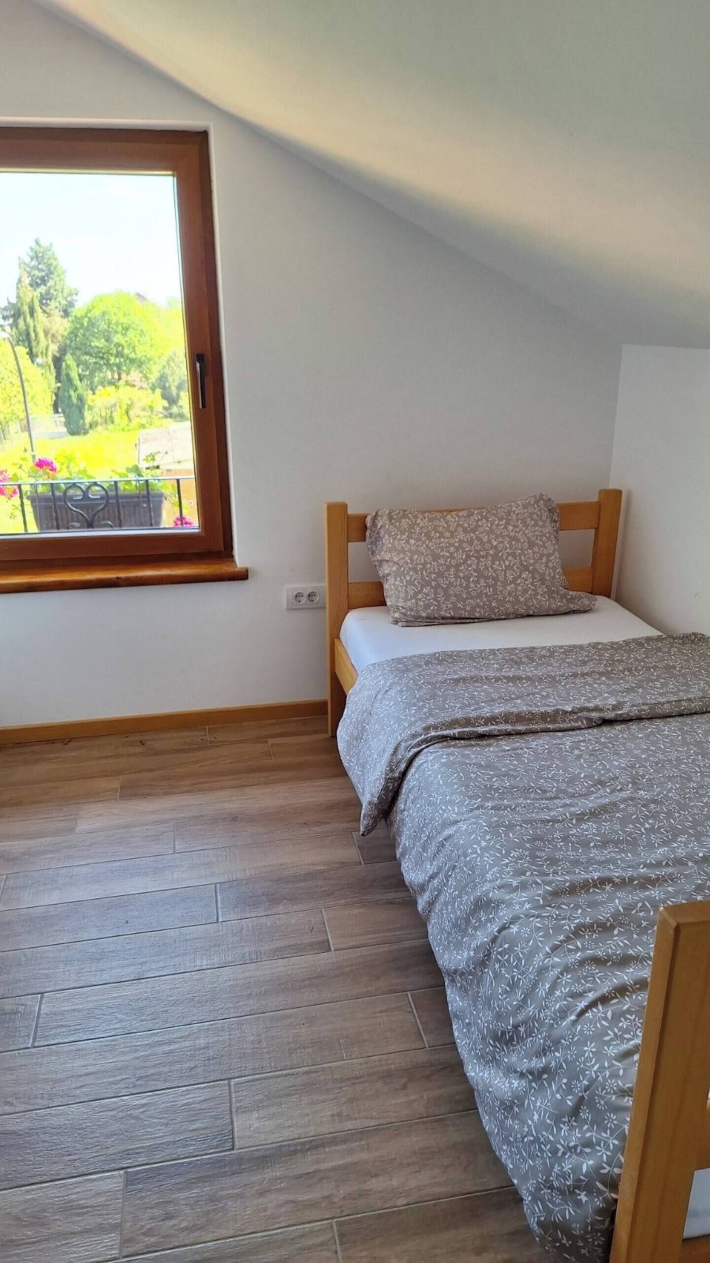 A bedroom with a wooden bed, a window with a view of greenery, and a herringbone-patterned floor.