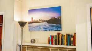 Una estantería con libros y una esfera decorativa, un cuadro de un paisaje fluvial y una lámpara de pie.