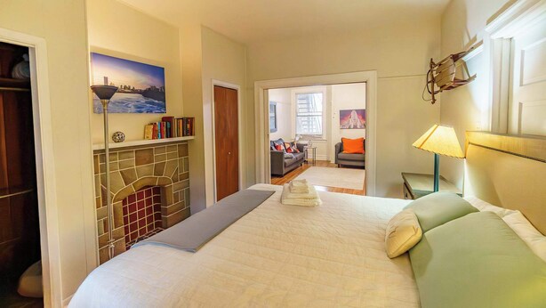Habitación de hotel con cama, chimenea, estantería y vistas al pasillo.