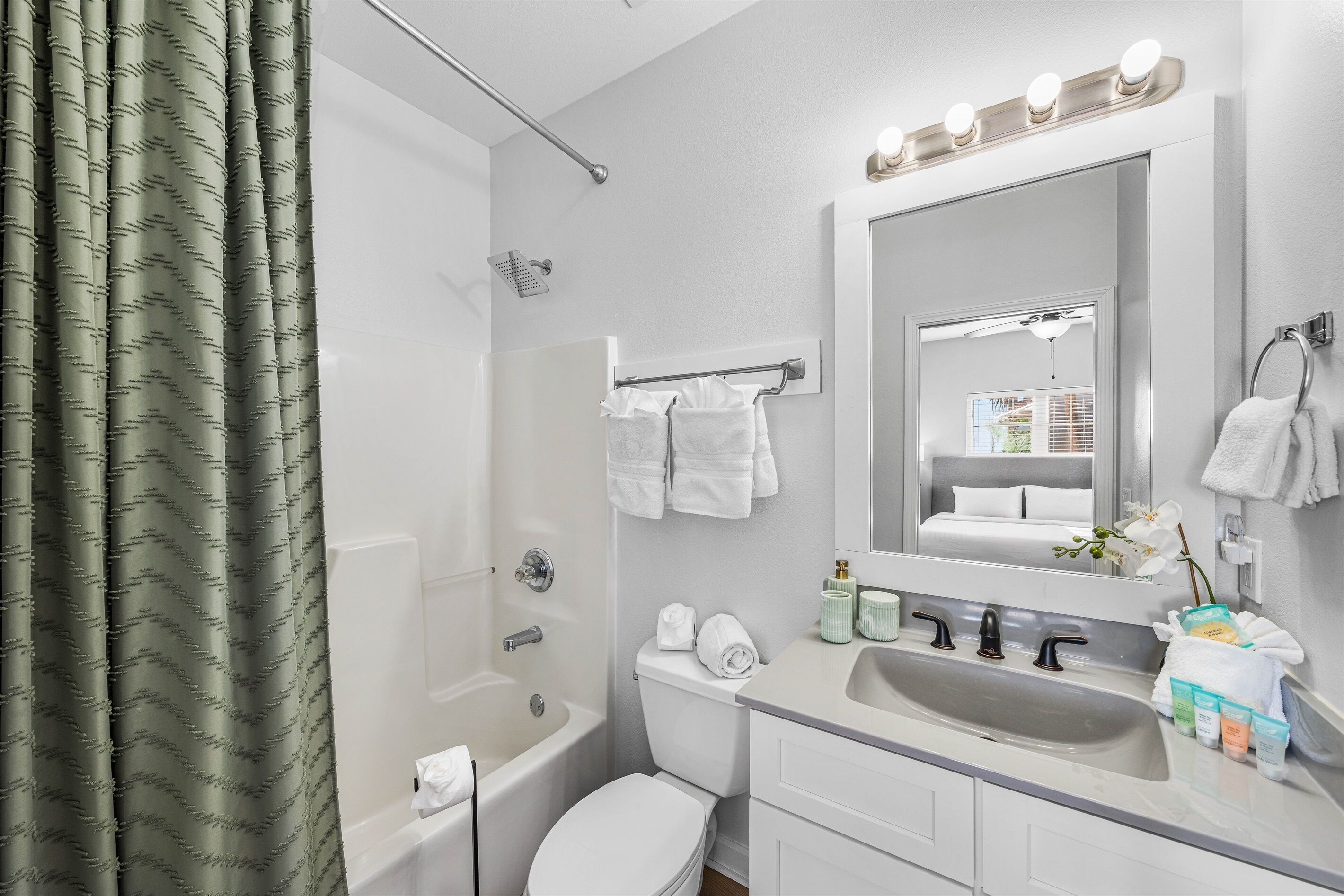 A modern bathroom with a bathtub, toilet, sink, and a large mirror with lights.
