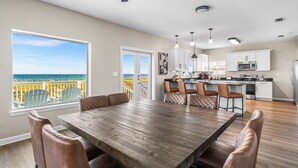 A spacious dining area with a large wooden table and leather chairs, a kitchen with white cabinets and stainless steel appliances, and a view of the ocean through large windows. - Lowe Tide, Fantastic Private Beach Front Home. 5 Stars! (Navarre)