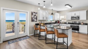 A modern kitchen with white cabinets, a large island with bar stools, a view to the beach, and a deck with a grill. - Lowe Tide, Fantastic Private Beach Front Home. 5 Stars! (Navarre)