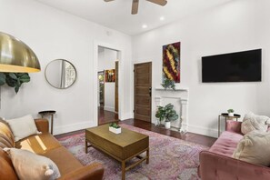 A spacious living room with a fireplace, a large TV mounted on the wall, and a modern ceiling fan.