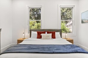 A bedroom with a bed, two nightstands, a window, and a painting on the wall.