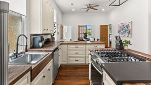 A modern kitchen with white cabinets, a stainless steel sink, a gas stove, and wooden countertops. - Marigny Retreat | Steps to Trolley, French Quarter (New Orleans)