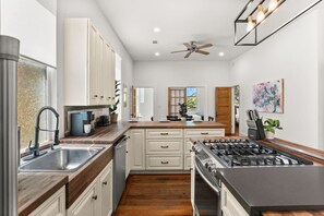 A modern kitchen with white cabinets, a stainless steel sink, a gas stove, and wooden countertops. - Marigny Retreat | Steps to Trolley, French Quarter (New Orleans)