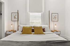 A modern bedroom with a large bed, two bedside tables with lamps, and framed artwork on the walls.