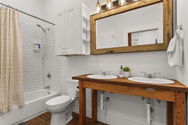 A bathroom with a shower, toilet, and two sinks with a wooden vanity.