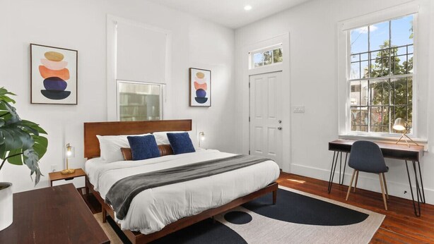 A bedroom with a bed, bedside table, desk, chair, and a large window. - Marigny Retreat | Steps to Trolley, French Quarter (New Orleans)