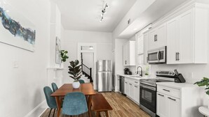 Une cuisine moderne avec des meubles blancs, des appareils en acier inoxydable et une table à manger en bois, accompagnée de chaises.