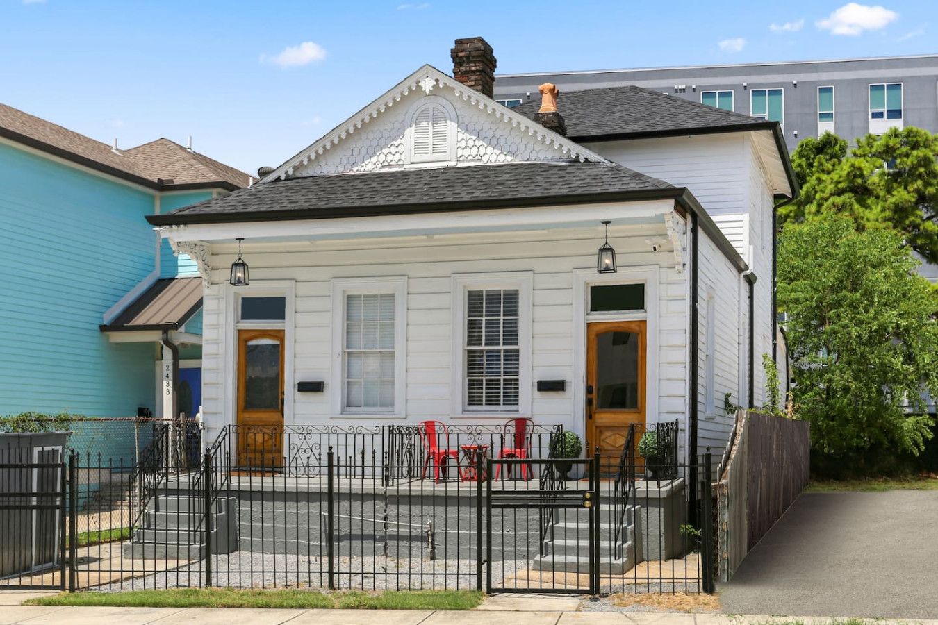 A white two-story house with a black metal fence, a red chair, and a wooden door.