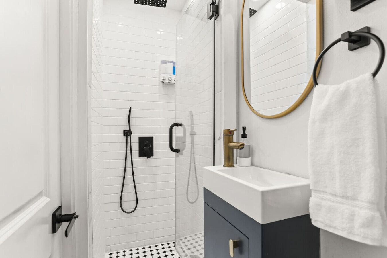 A modern bathroom with white tiled walls, a white sink with a gold faucet, a towel hanging on a towel rack, and a shower with a handheld showerhead.