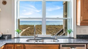 A kitchen with a large window overlooking a beach.