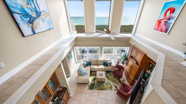 A spacious interior with a high ceiling, a balcony with a view of the ocean, and a seating area with a coffee table.
