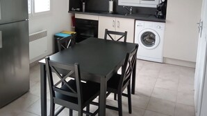 A compact kitchen with a dining table, chairs, a washing machine, and a refrigerator. - Maison en Bordure de mer (Sotteville-sur-Mer)