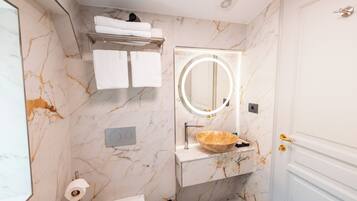 Une salle de bain avec des murs en marbre, un lavabo avec un receveur, un miroir avec un éclairage intégré et un porte-serviettes.