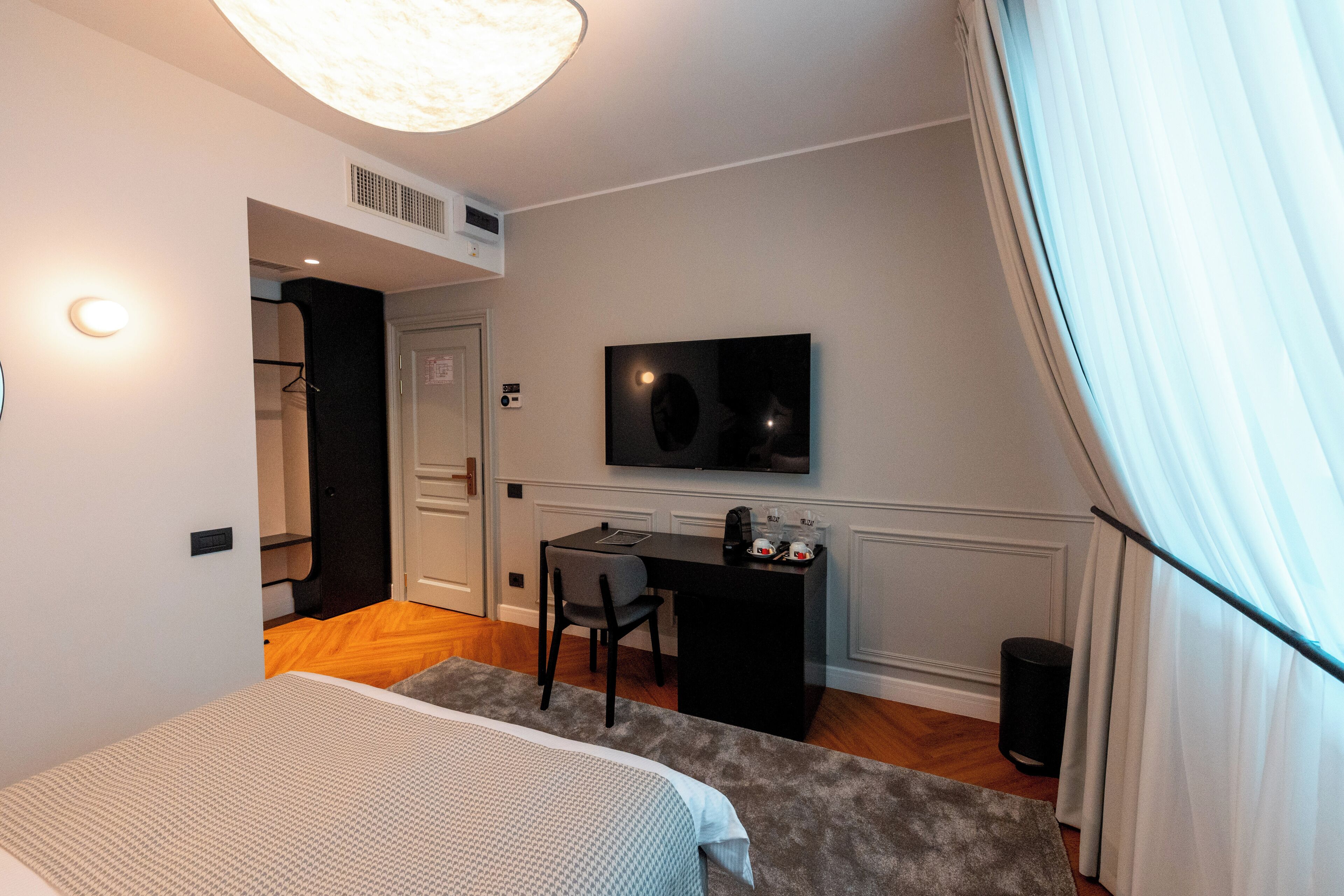 A bedroom with a bed, a desk, a chair, a television, and a window with curtains.