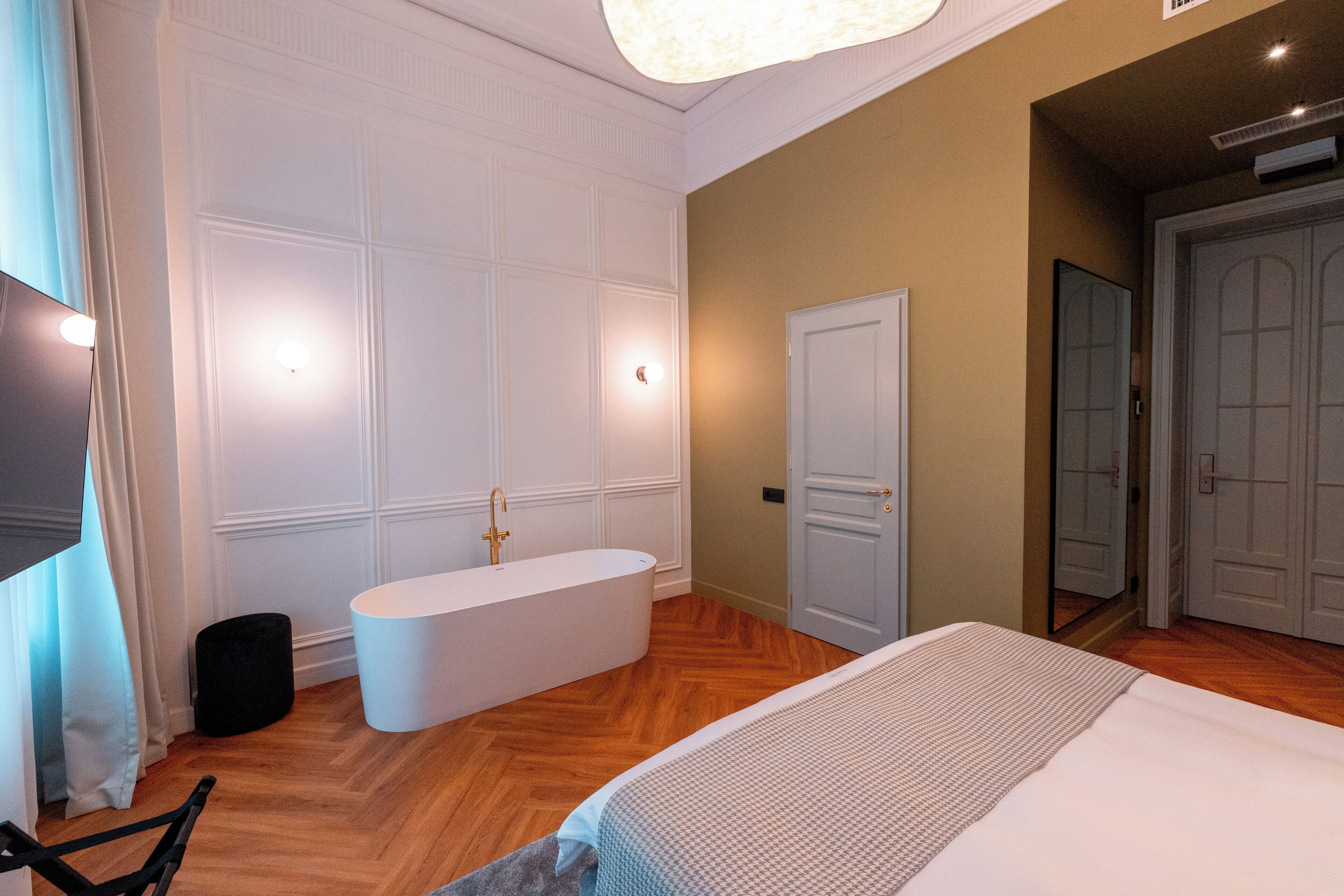A modern hotel room with a large bed, a bathtub, and a wardrobe.