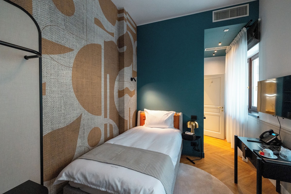A hotel room with a bed, a desk, a chair, a TV, and a window with curtains.