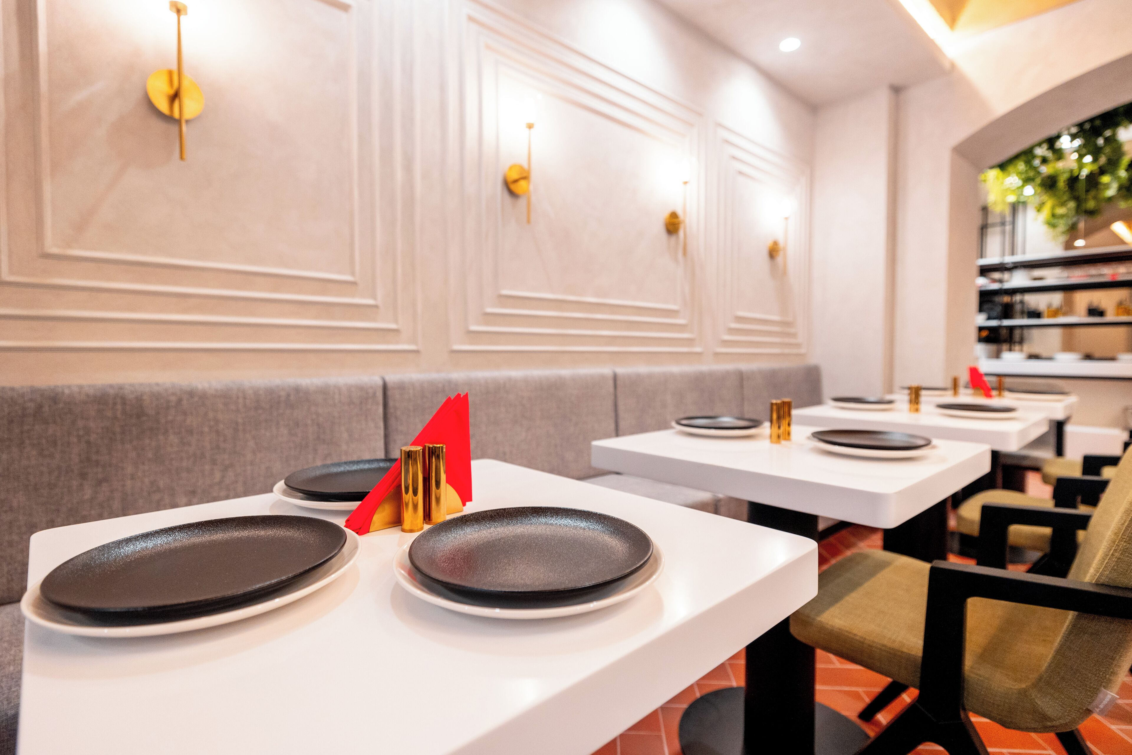 Een restaurantinterieur met witte tafels, zwarte borden en rode servetten.