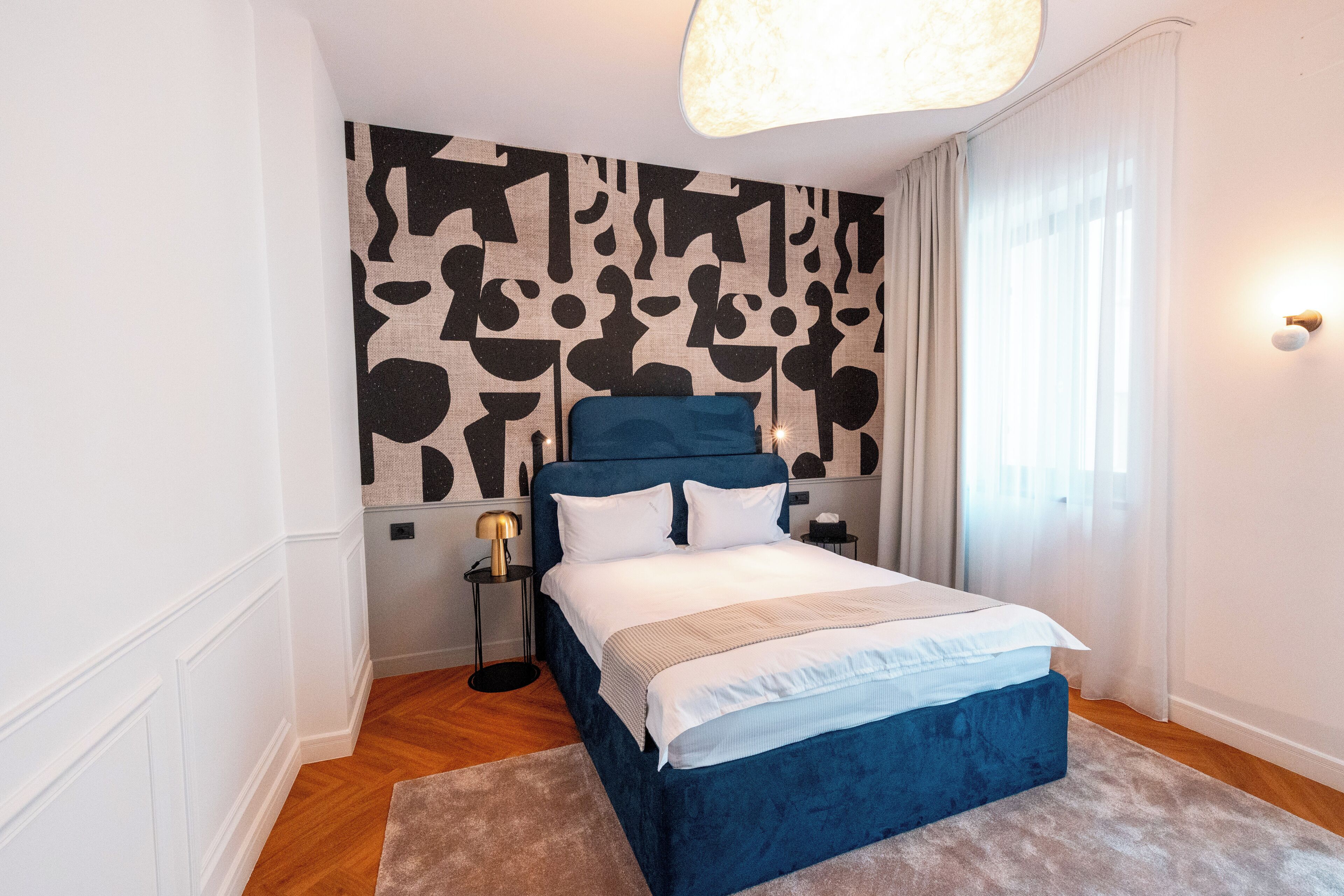 Un dormitorio moderno con una cama grande, un papel tapiz estampado y una mesita de noche con lámpara.
