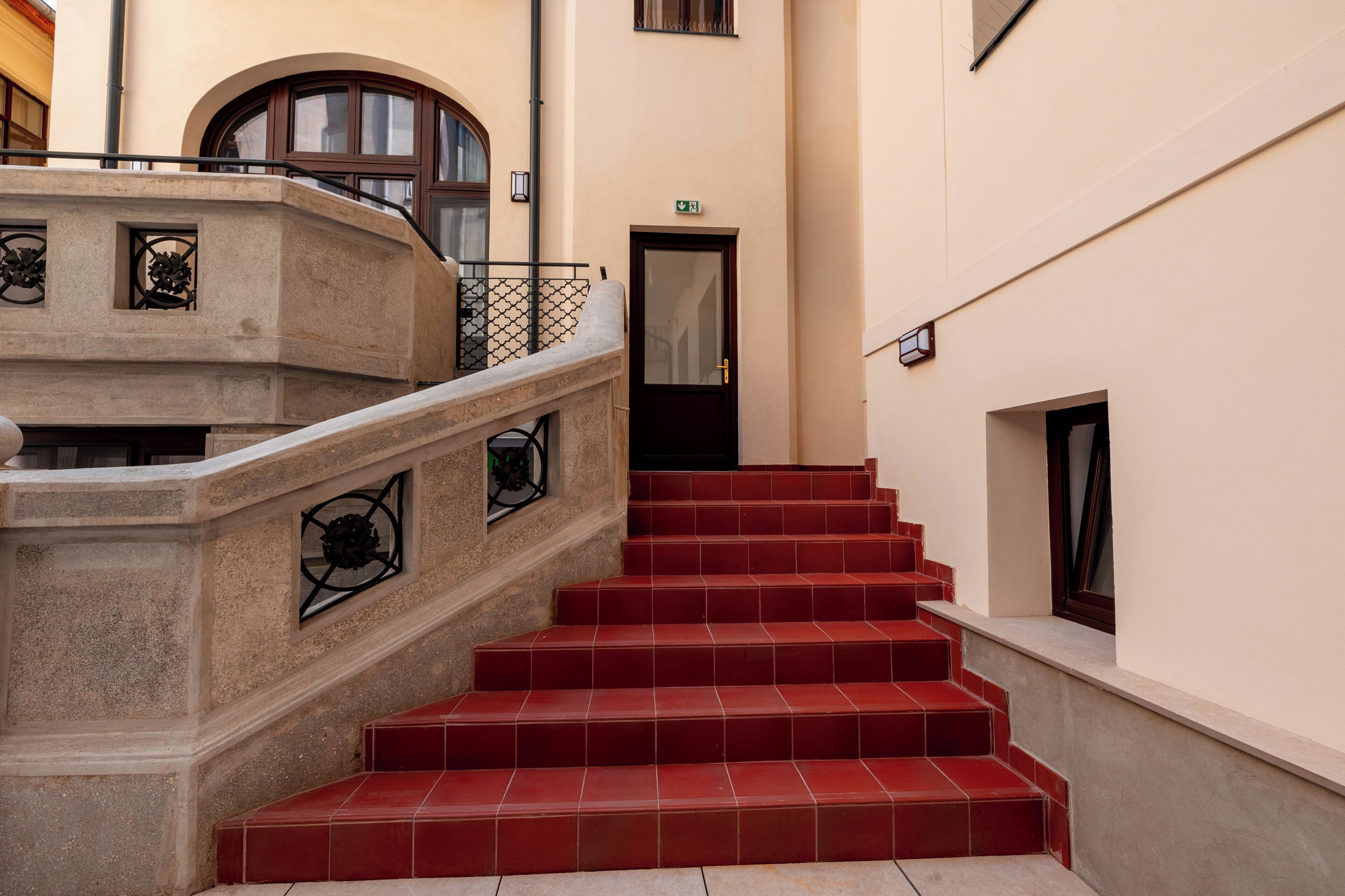 Un escalier à marches recouvertes de tuiles rouges menant à une porte sur laquelle est apposée une enseigne verte indiquant la sortie.