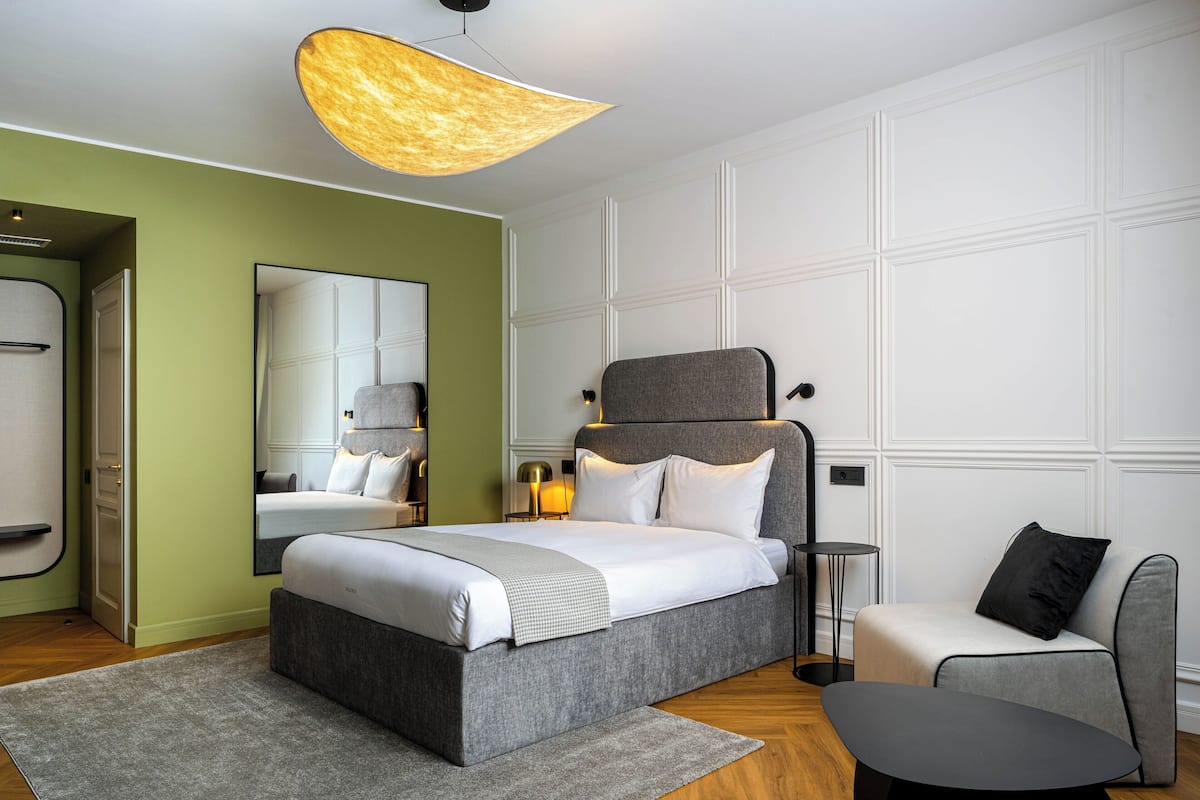 A modern bedroom with a large bed, bedside tables, a chair, and a unique ceiling light fixture.