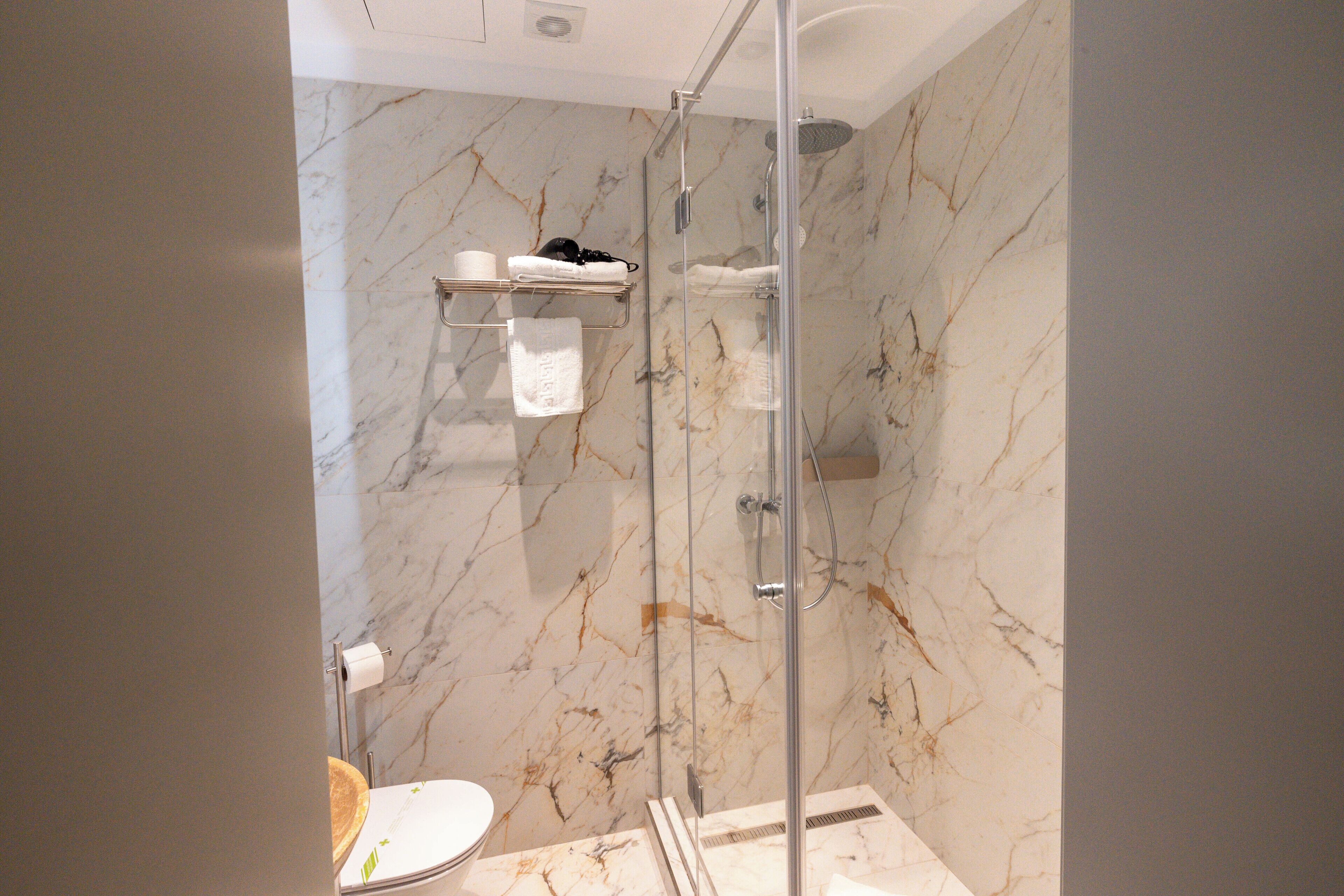 A bathroom with a shower, toilet, and marble walls.