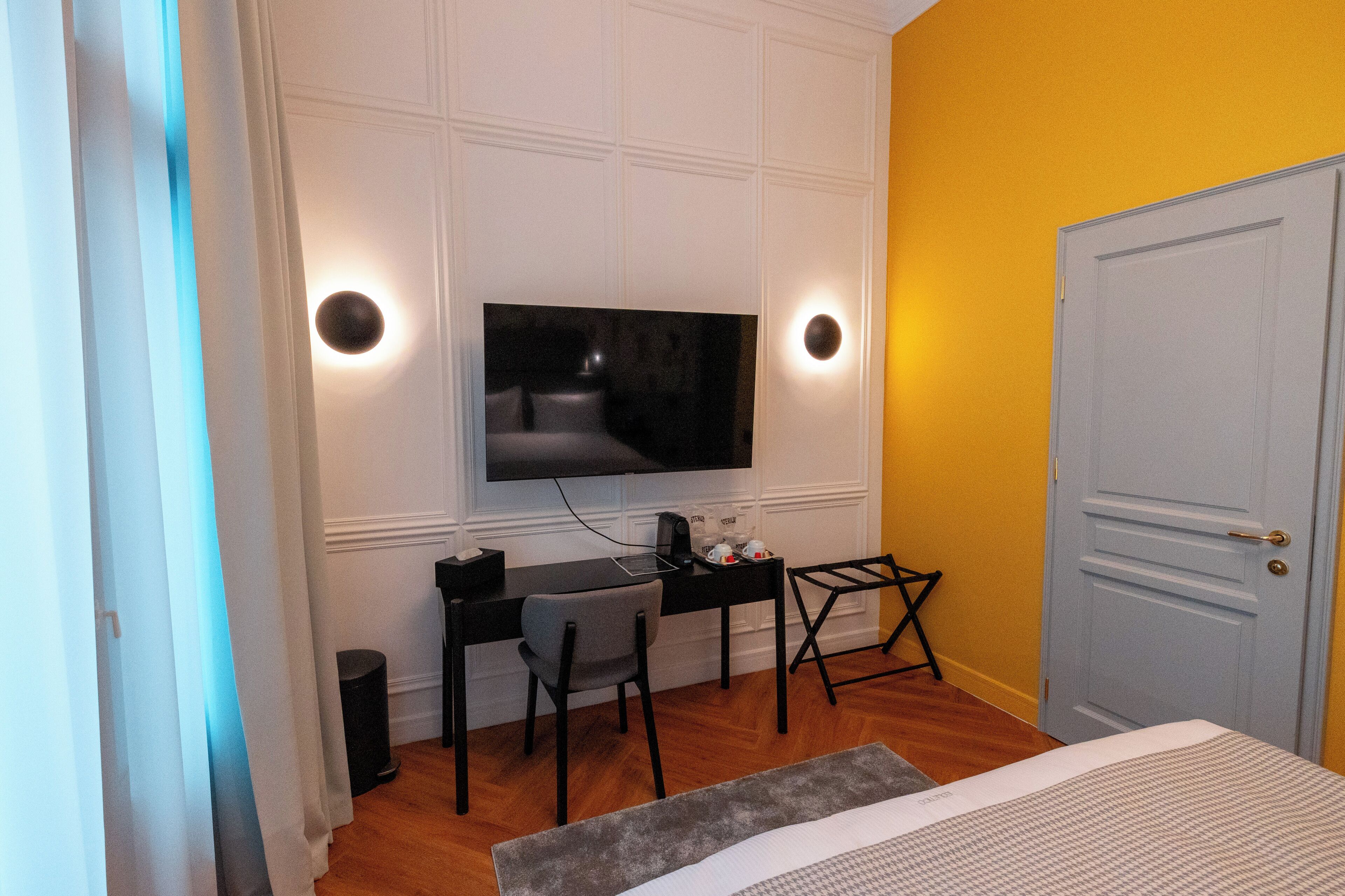 Un dormitorio con cama, escritorio con silla, televisor montado en la pared y una puerta.