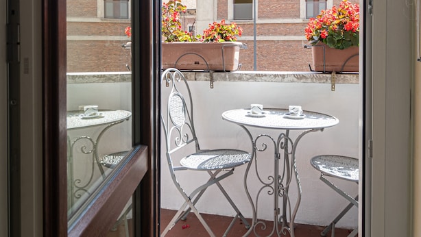 A balcony with two metal tables and chairs, potted plants, and a view of a brick building with windows. - Italianway Easy - Cipro 5 (Milan)