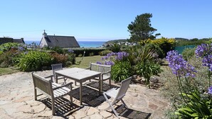 An outdoor patio with a table and chairs, surrounded by a garden with various plants and flowers. - 391-Beautiful fisherman's house, closer to the beach with sea view (Primelin)
