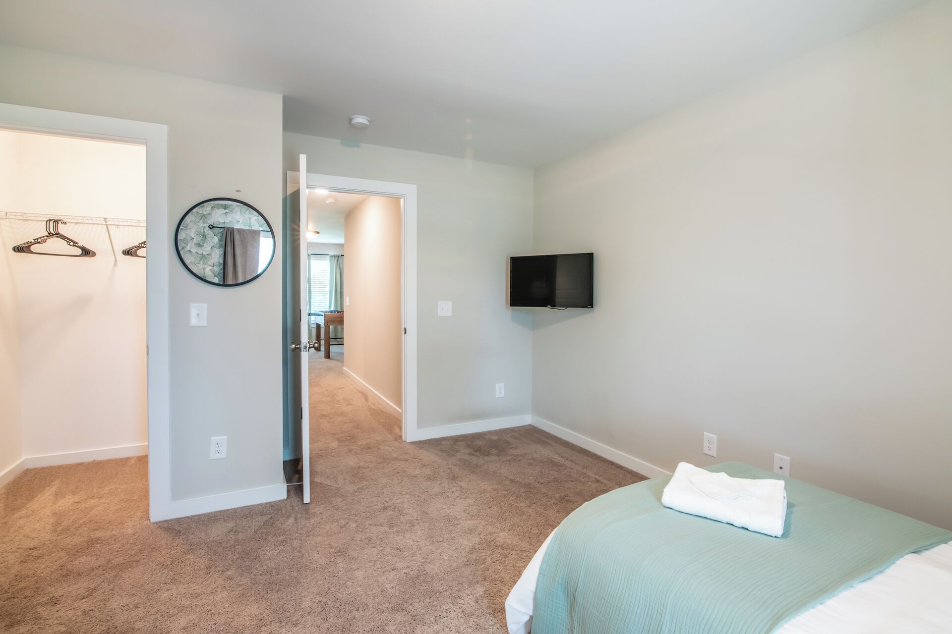 A bedroom with a bed, a television mounted on the wall, and a hallway leading to another room.