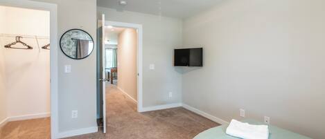 A bedroom with a bed, a television mounted on the wall, and a hallway leading to another room.