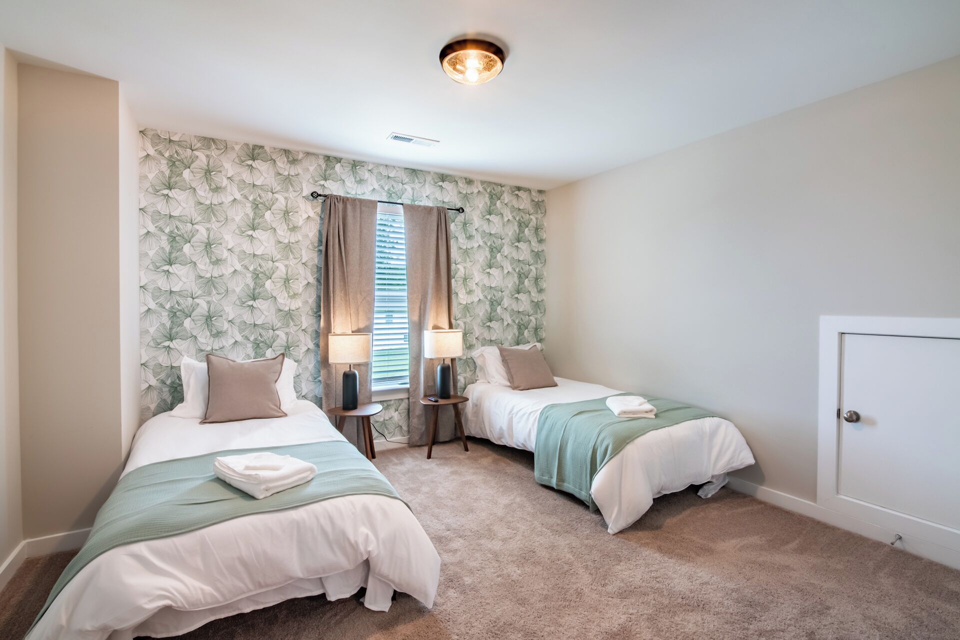 Ein Schlafzimmer mit zwei Betten, einem Fenster mit Jalousien, einer Tür und einer Deckenleuchte.