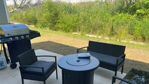 Une terrasse extérieure équipée d’un barbecue, de deux chaises, d’une table ronde et d’une petite table.