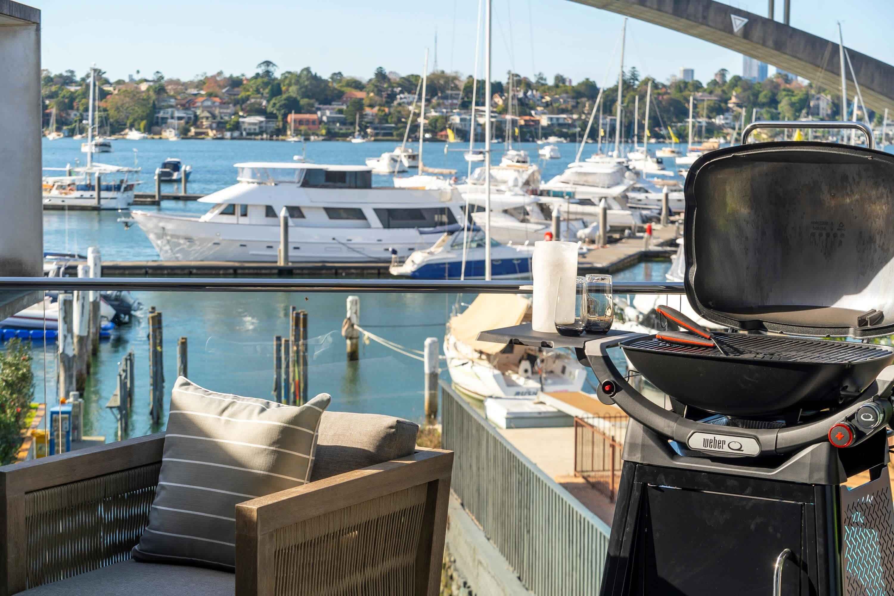 A balcony with a grill, a wicker chair, and a view of a marina with boats.