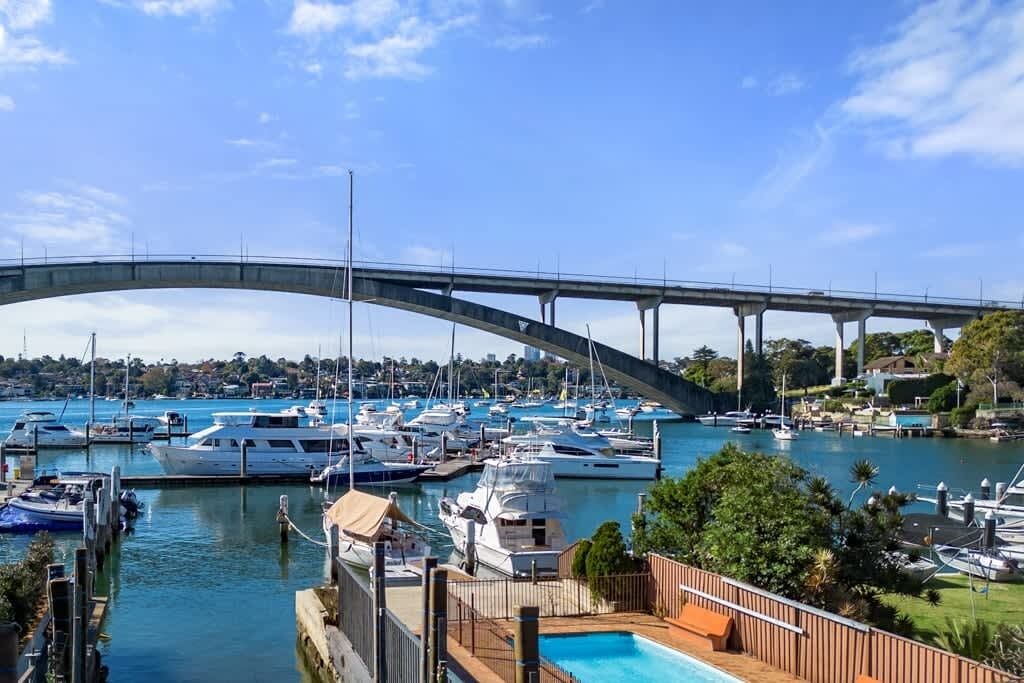 A marina with boats docked, a bridge in the background, and a pool area with a fence.