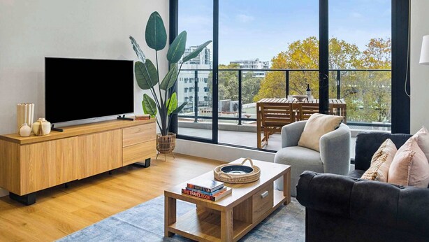 Un soggiorno moderno con una grande televisione, mobili in legno, un tavolino da caffè con libri e un balcone con tavolo e sedie.