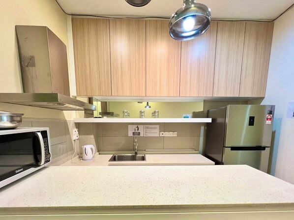 A modern kitchen with wooden cabinets, a stainless steel refrigerator, a microwave, and a sink.