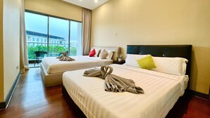 Habitación de hotel con dos camas, ventilador de techo y un ventanal con vistas a edificios y follaje.