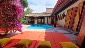A pool area with red lounge chairs and yellow cushions, surrounded by a tiled patio and a building with wooden doors. - La Villa Mandragore (Hyères)