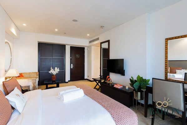 A hotel room with a large bed, a desk with a chair, a TV, a mirror, and a potted plant. - Spectacular Suite JW Marriott Marina (Dubai)