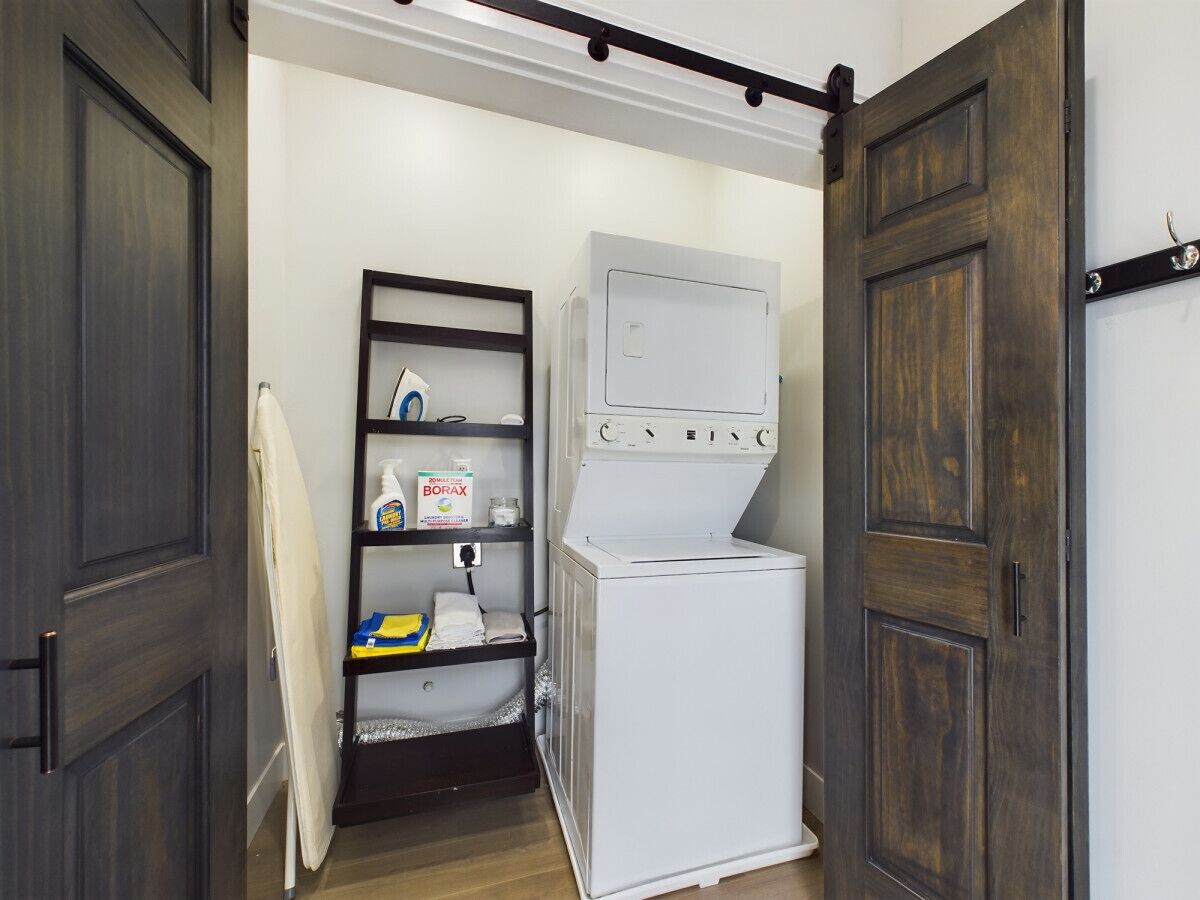 A laundry room with a washing machine, a shelf with cleaning supplies, and a door.