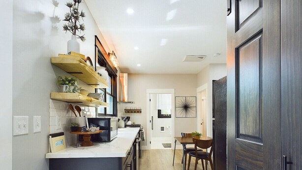 A compact kitchen with a central island, wooden shelves, and a dining area with a table and chairs.