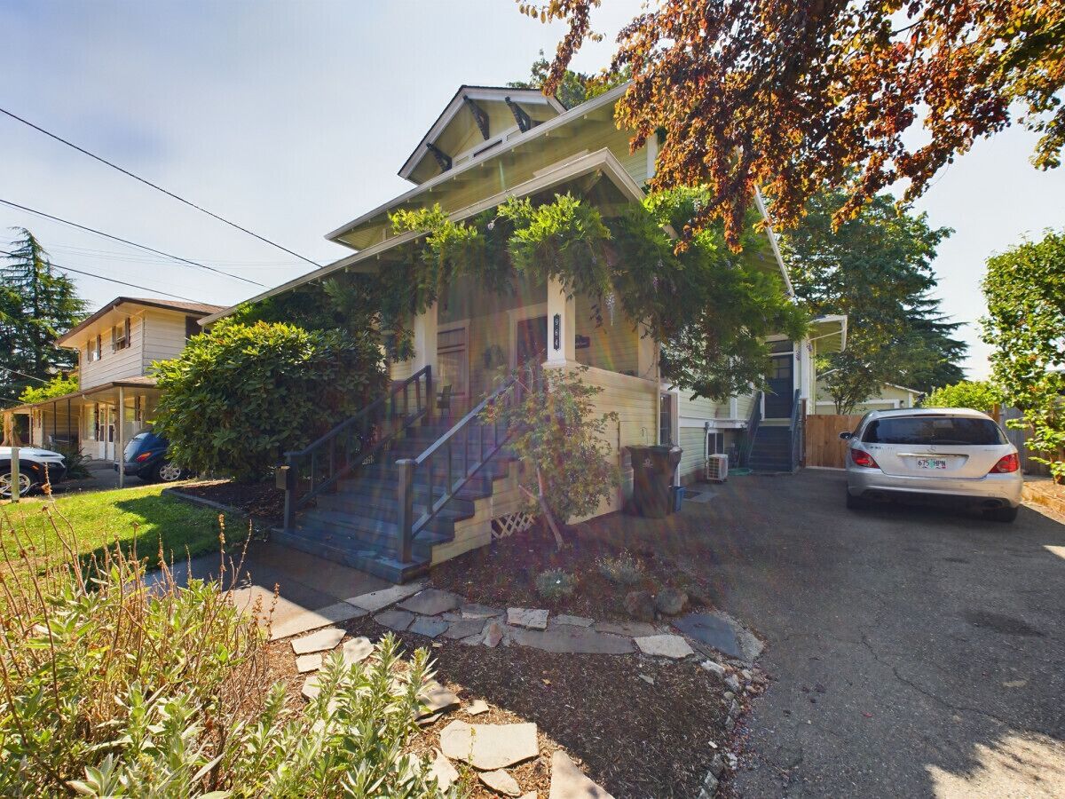 A residential house with a front yard, a staircase leading to the entrance, and a parked car.