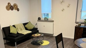 En moderne stue med en sort sofa, et sofabord og et spiseområde med en stol og et bord.